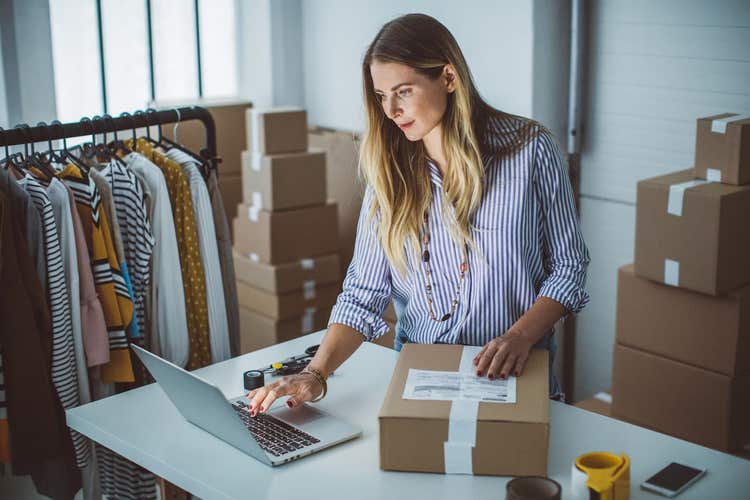 Femme utilisant un ordinateur portable, entourée de boîtes d'inventaire.