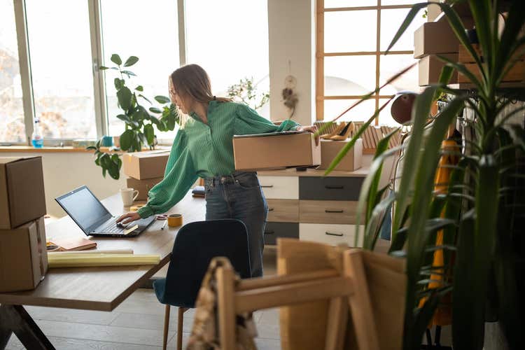 Propriétaire d'une petite entreprise travaillant sur un ordinateur portable, entouré de cartons remplis d'inventaire.