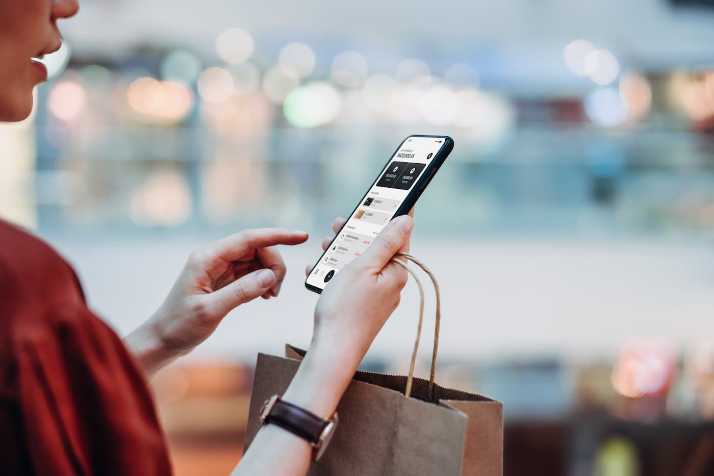 Femme avec un sac de courses à la main, regardant des transactions en ligne sur son téléphone