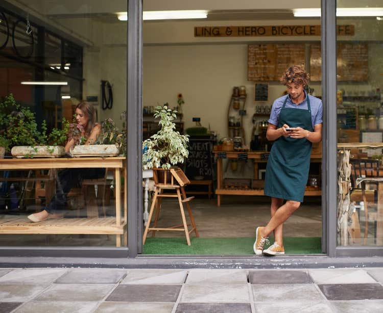 Man standing infront of a cafe looking at his phone.
