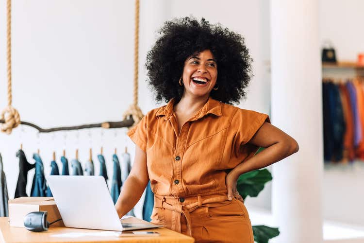 Female small business owner smiling in front of her laptop inside retail store.