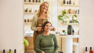 Two women in a salon, with one styling the other’s hair. Clover POS in the background.