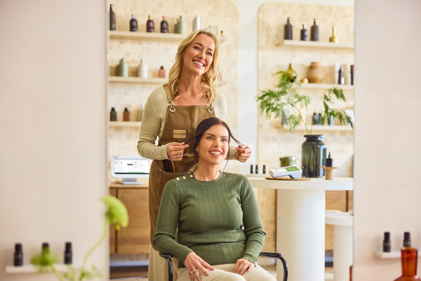 Two women in a salon, with one styling the other’s hair. Clover POS in the background.