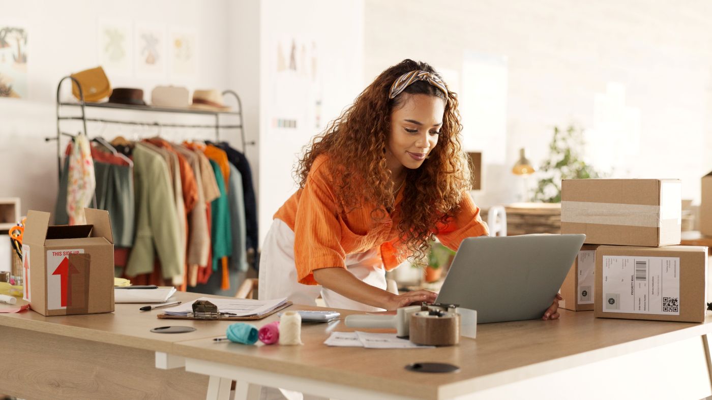 Female business owner working on her laptop and managing stock inside her boutique