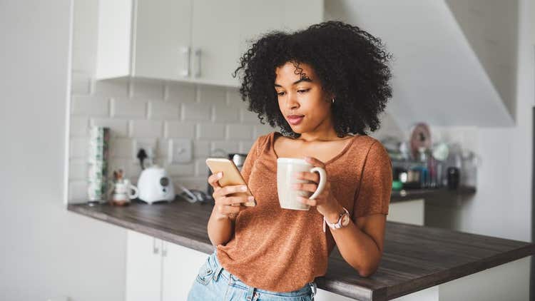 Woman scrolling on phone holding mug