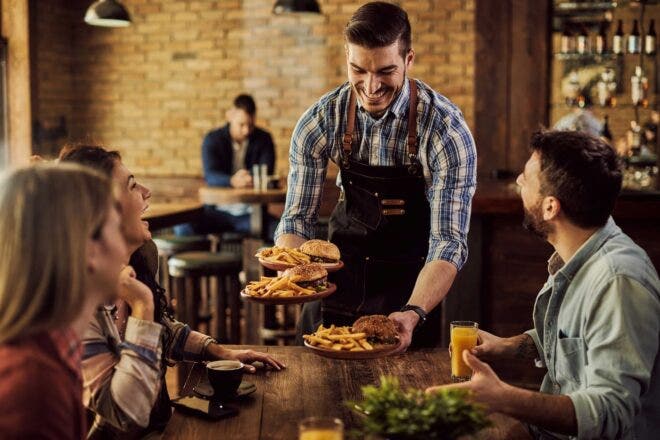 Happy waiter serving burgers and fries to table