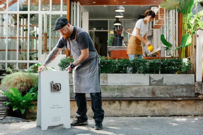 Coffee shop staff sprucing up the outdoor garden and setting the sign out front