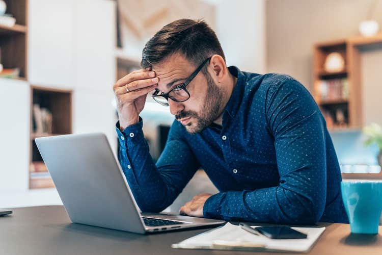 Worried man holding head looking at laptop