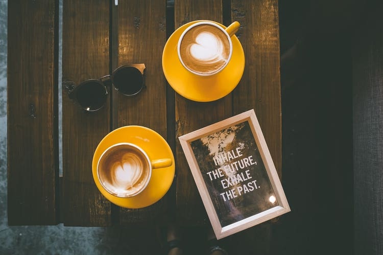Two cups of coffee on a table with an inspirational sign