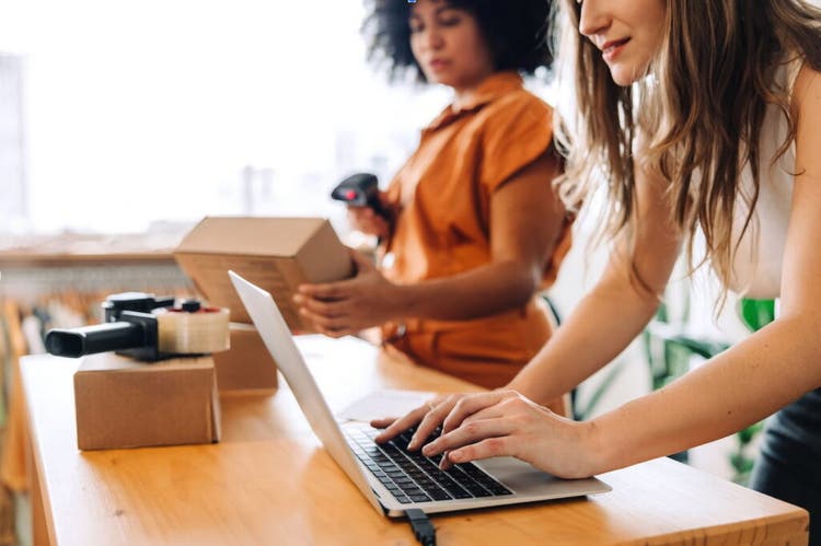 Women scanning box with barcode scanner and woman working on a laptop