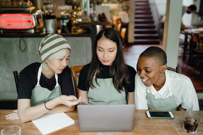Three restaurant employees sitting at a table in the restaurant with notepad and laptop