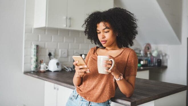 Woman scrolling on phone holding mug