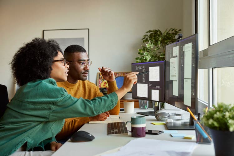 Two professional service providers collaborating at a dual-monitor workstation in a modern office to streamline operations.