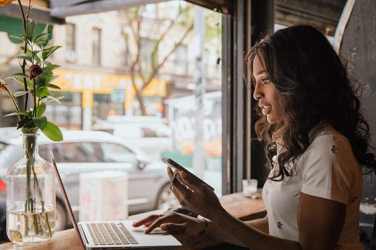 Black woman looking at laptop and holding phone