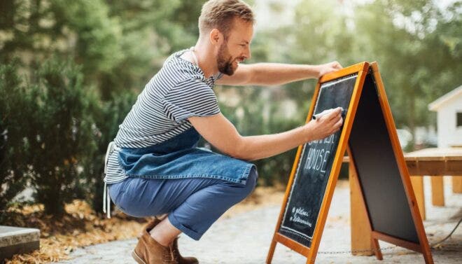 Restaurant owner writing on sidewalk sign
