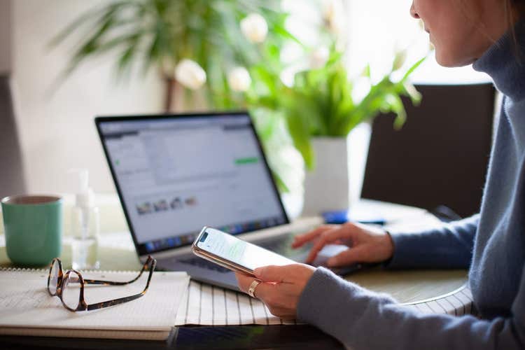 Woman looking at laptop and holding phone