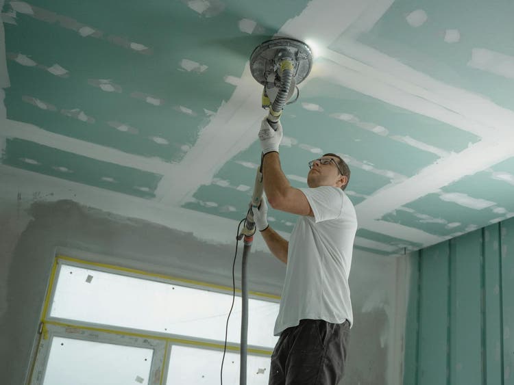 Painter sanding ceiling inside a home