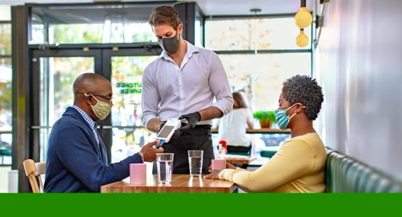 Mask waiter holding a Clover Flex for customer to insert credit card.