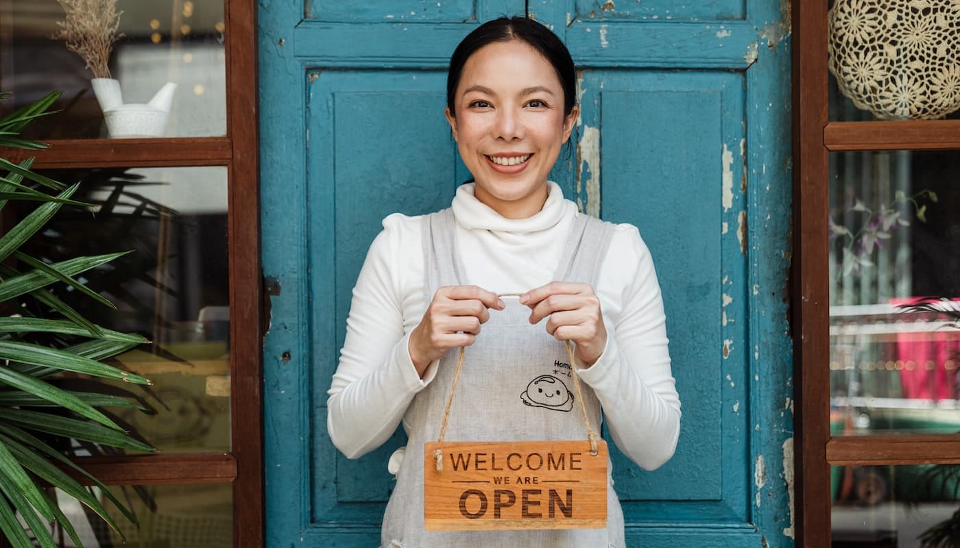 happy store owner holding welcome sign