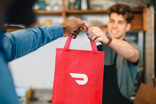 Restaurant employee handing Doordash bag to delivery person