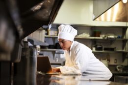 Female chef in commercial kitchen using laptop