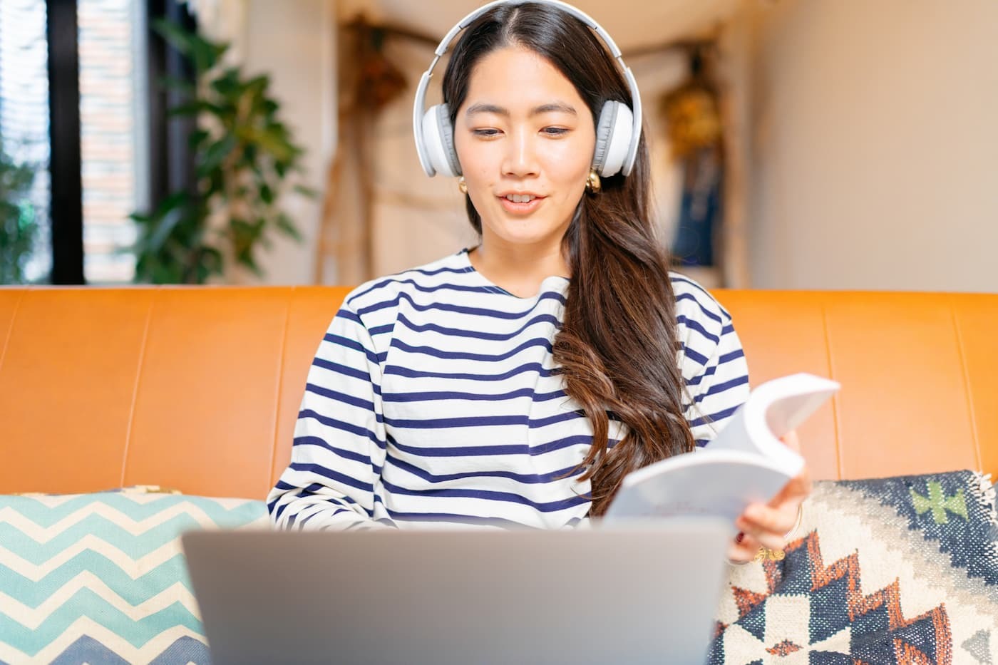 Woman wearing headphones holding book and laptop