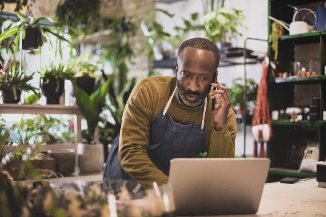 Plant shop owner on phone looking at laptop
