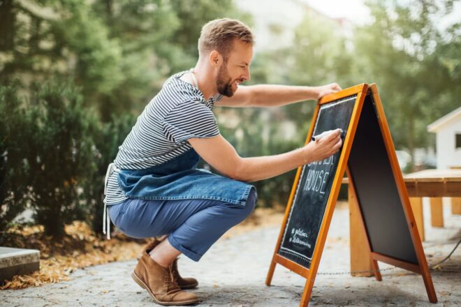 Man writing on chalkboard outside business