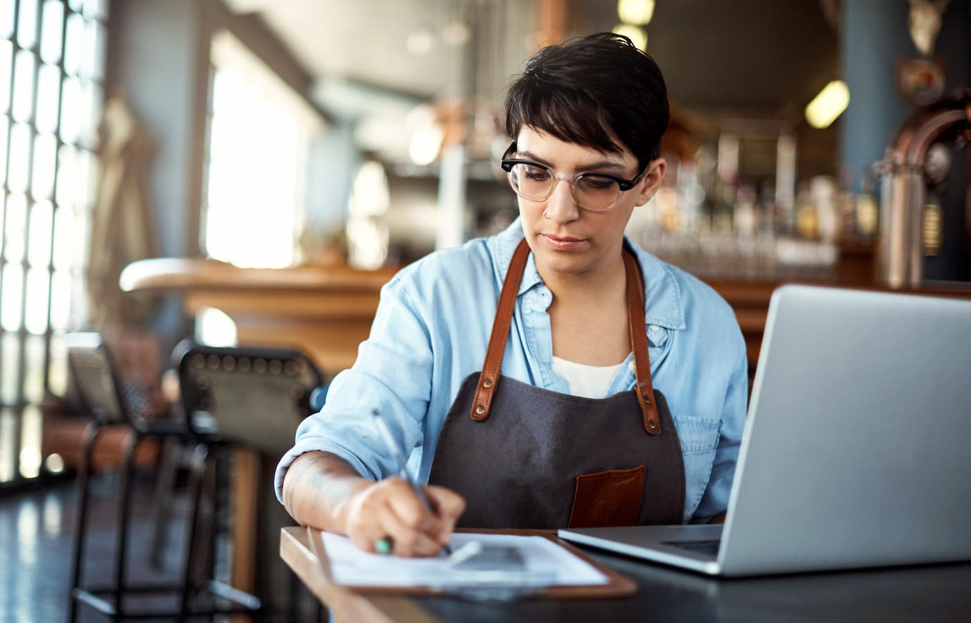 Restaurant owner writing on clipboard by laptop