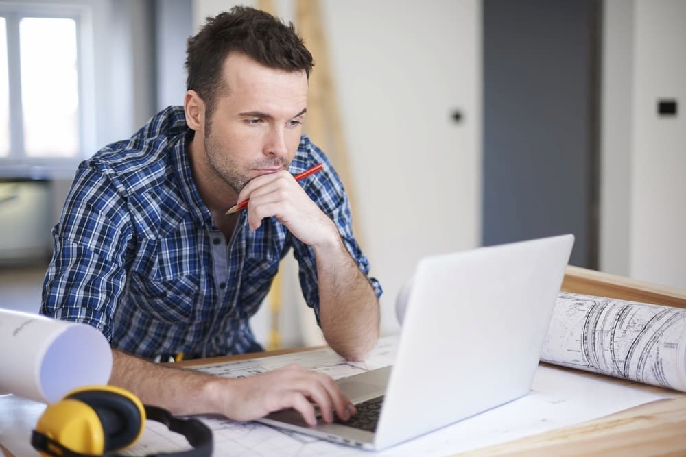 Man looking at laptop with blueprints on desk