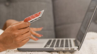 Online shopper holding credit card while shopping on laptop