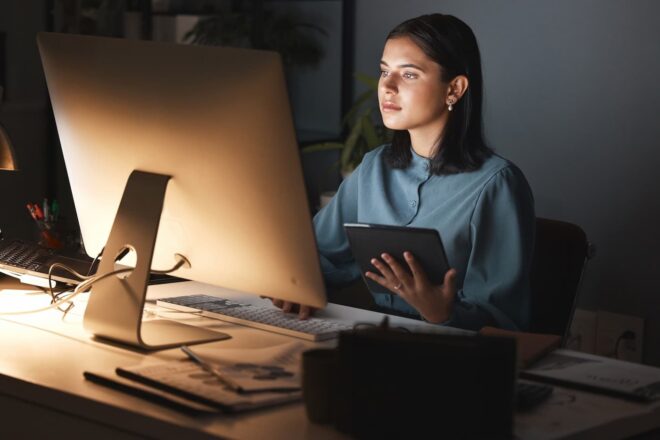 Woman looking at desktop monitor holding tablet