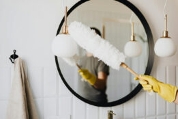 Person wearing yellow cleaning gloves and cleaning bathroom mirror