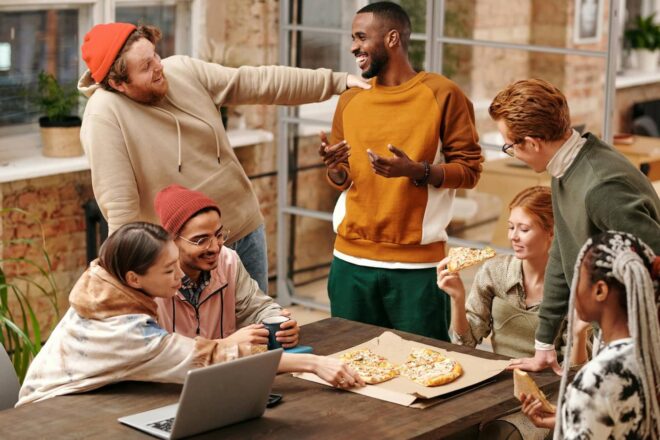 Group of employees smiling, eating pizza, and talking