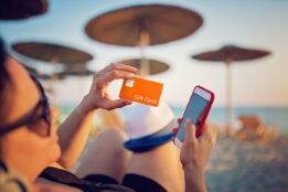 Woman sitting on the beach using a gift card as she makes a purchase on her mobile phone
