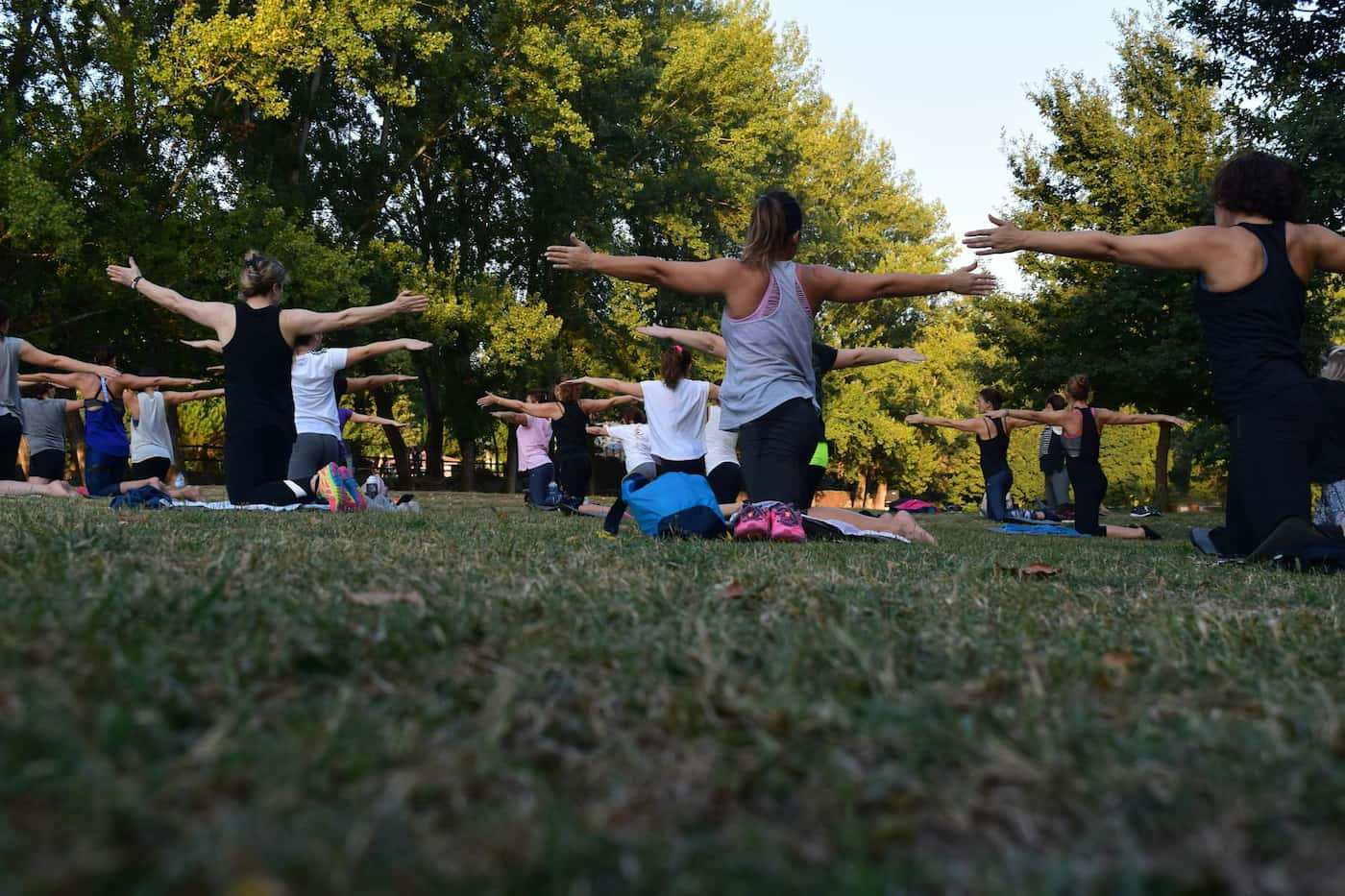 Pilates instructors leading an outdoor fitness class to adults on mats on the grass surrounded by trees