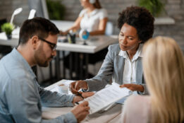 Female real estate agent sitting with a couple in an office while reading over a lease agreement with the couple.