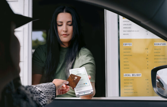 Man at a drive-through coffee restaurant tapping his credit card on a Flex Pocket while barista holds device at the window.