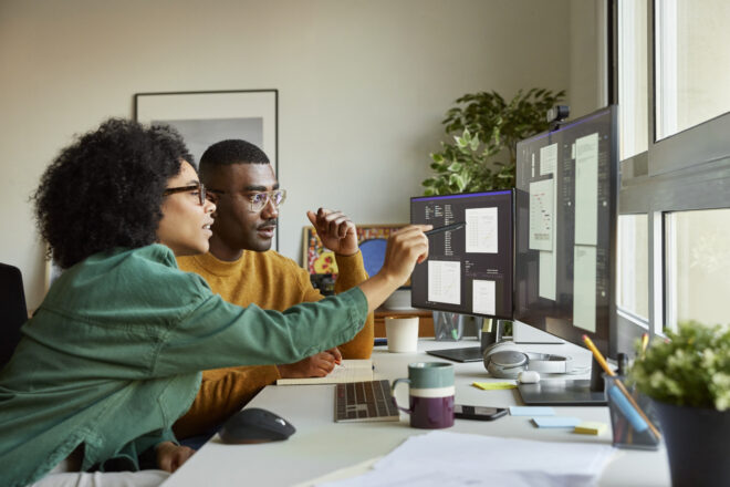 Two professional service providers collaborating at a dual-monitor workstation in a modern office to streamline operations.